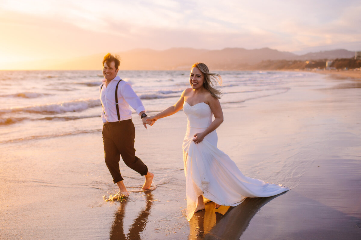 bride and groom run and smile on the beach during sunset