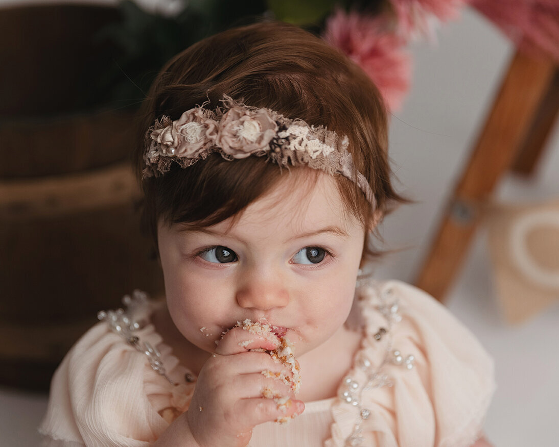 Toddler girl eats cake during her first birthday session in milestone baby picture in Murrysville portrait studio.