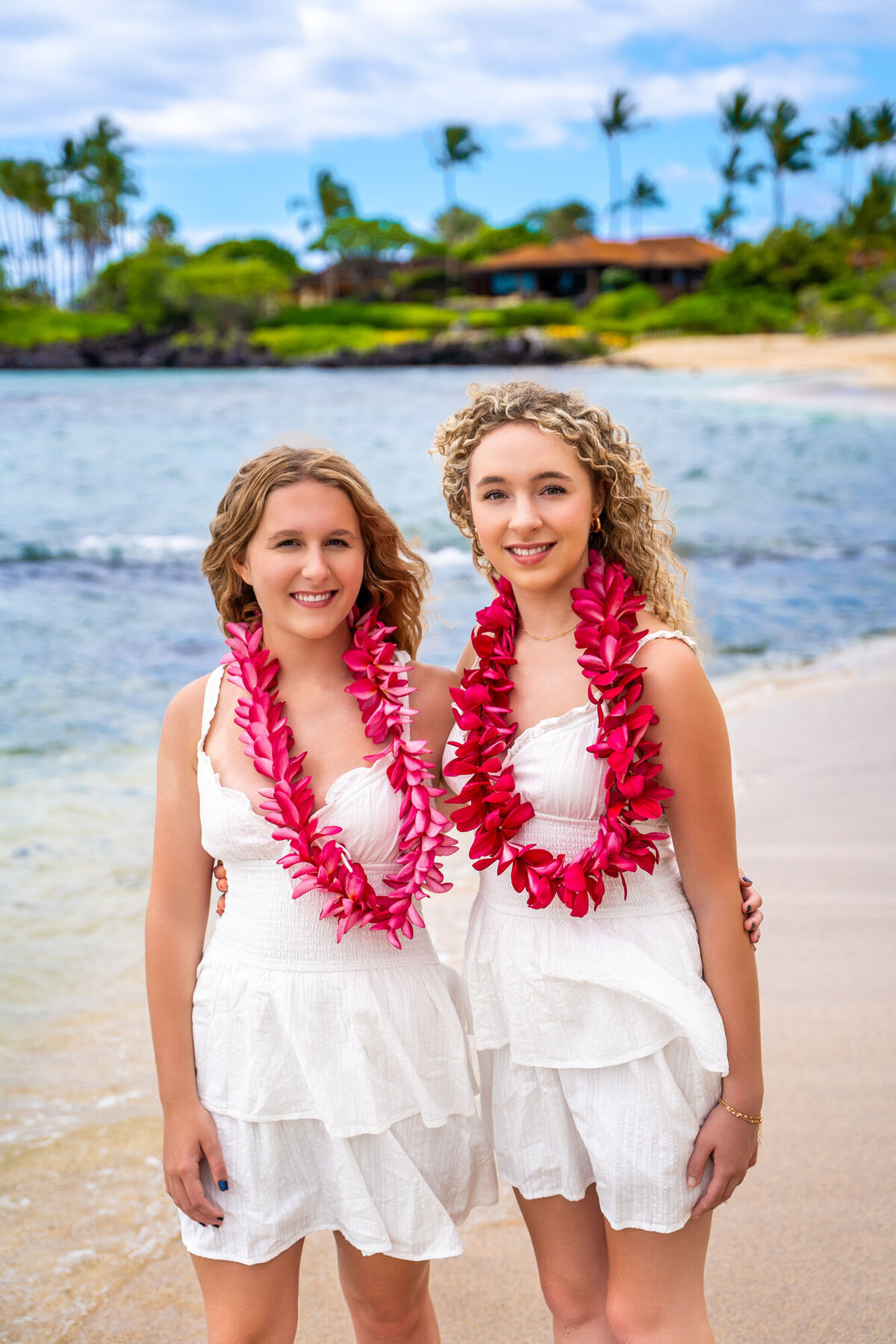 Two girls wearing pink flower leis on kukio beach, taken by big island family photographer