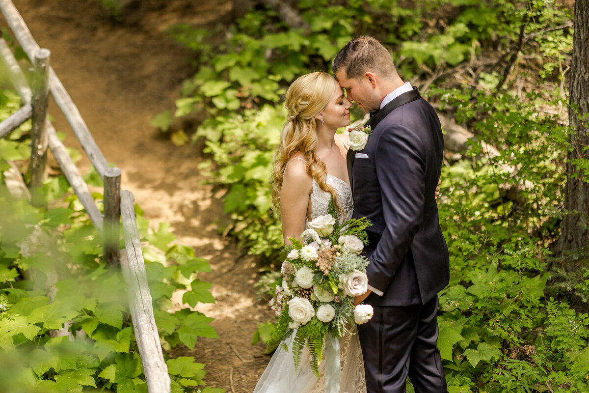 Bride and groom in forest near Tumalo Falls with bridal bouquet of roses and ferns