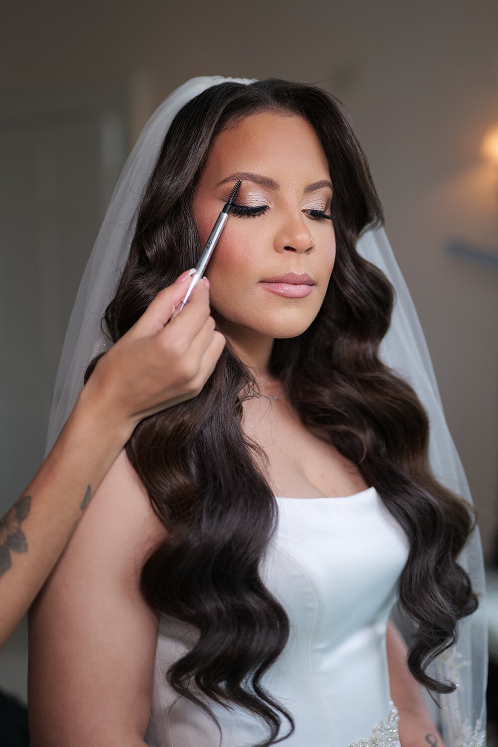 Expert professional makeup artist in NYC applying bridal makeup with a brush inside her studio, featuring a beautiful bride in an elegant white wedding dress.