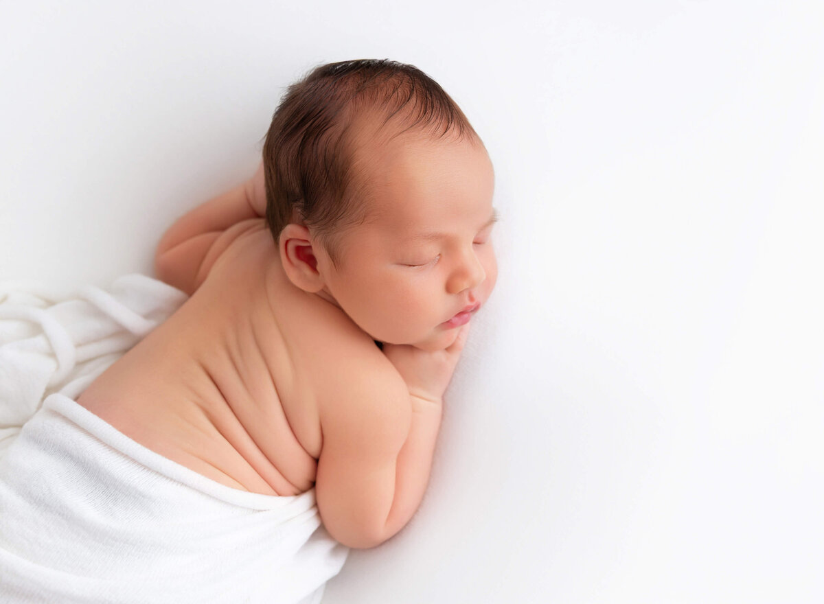 Modern NYC newborn photographer captures baby boy on white blanket 