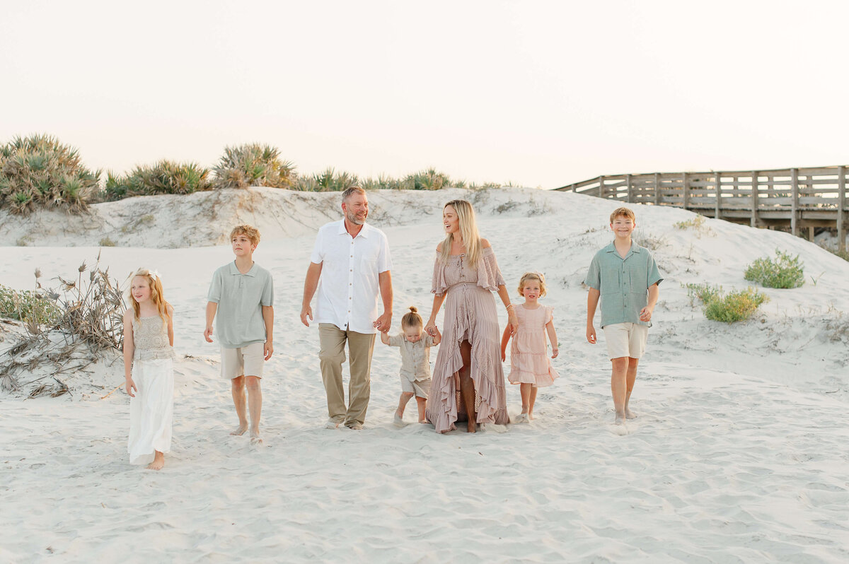 Family of 7 walks on the white sand near the dunes and boardwalk holding hands at sunset documented by a photographer in Kissimmee