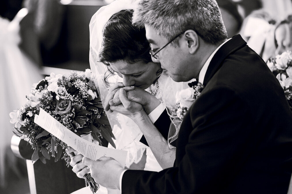 A bride kissing her groom's hand at their wedding.