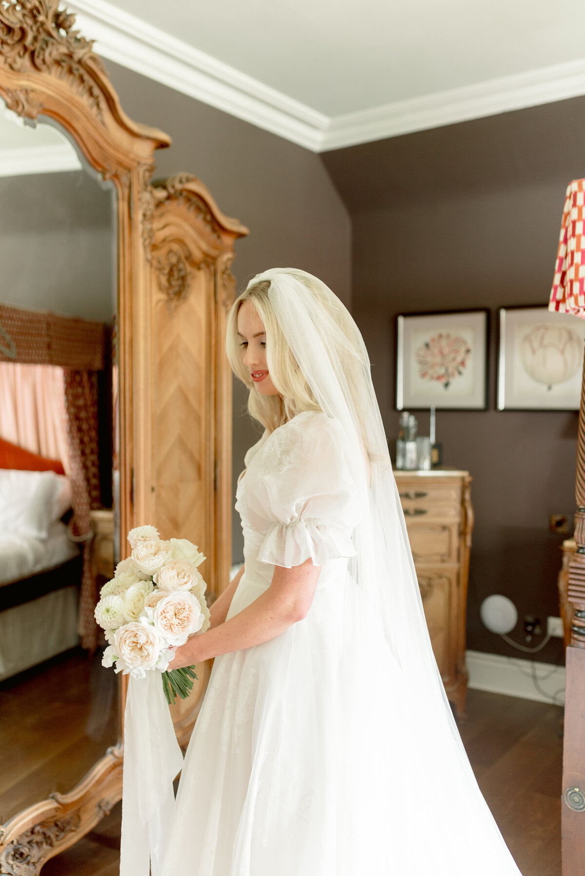 Beautiful wedding photograph of Bride in patterned silk wedding dress with puff sleeve, cathedral length veil and soft coral and ivory peony rose bouquet with satin ribbons in the Bridal Suite of Cromlix House, Scotland.