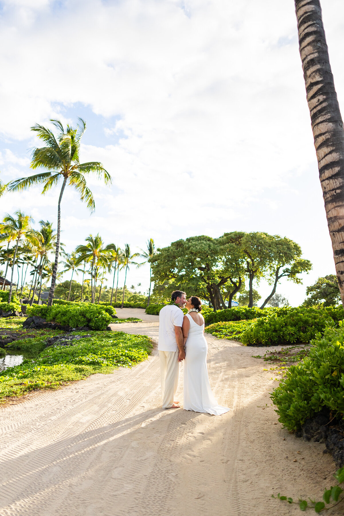 bride and groom white dress kissing with palm trees and sandy beach