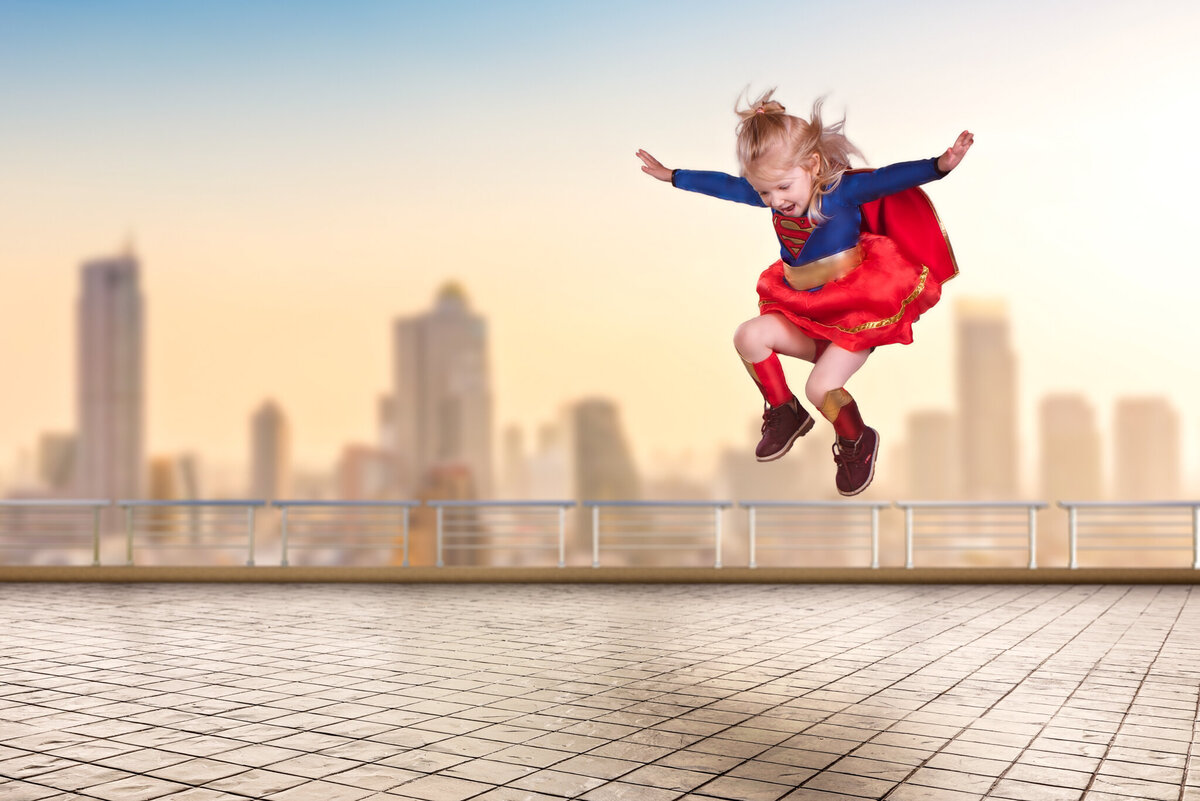 Dynamic portrait of a young child dressed as a superhero, leaping above an urban cityscape in a bold and imaginative pose. Captured in Overland Park, Kansas, this creative and empowering setup is perfect for families seeking unique child photography.