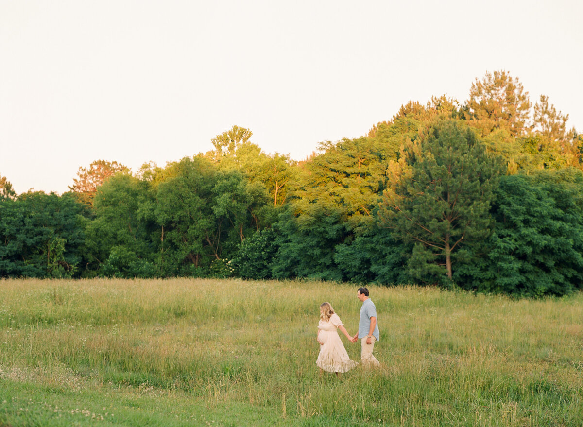 New parents walking in a field. Image by Raleigh maternity photographer A.J. Dunlap Photography.