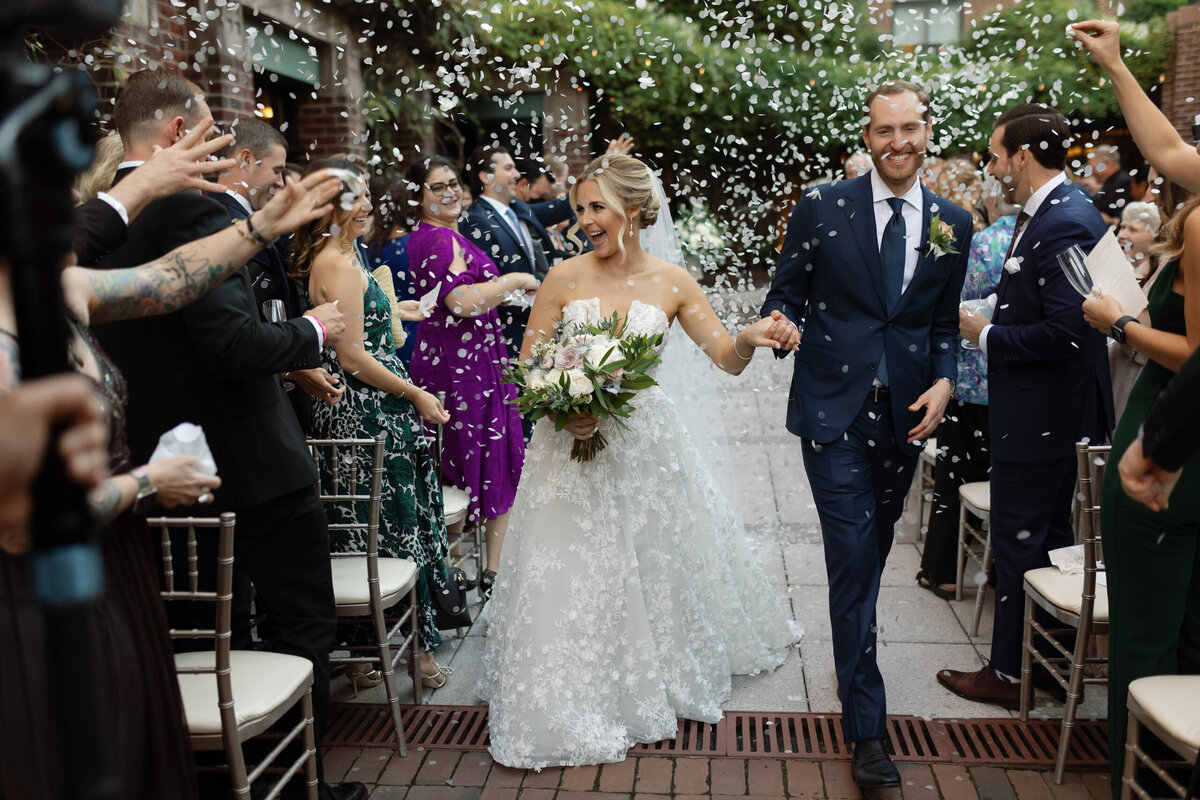 Bride and groom walk down the aisle with bubbles in a natural, joyful outdoor wedding.