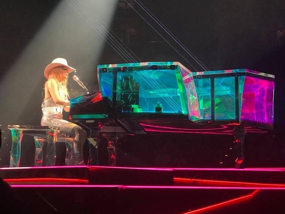 photo of Lady Gag playing clear glass reflective multi colored piano at a concert