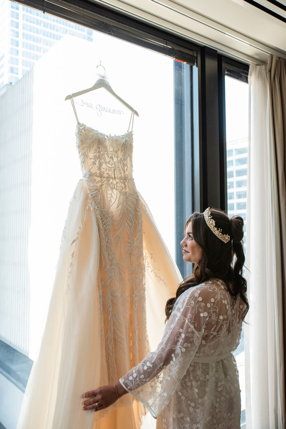 A bride is looking at her wedding dress hanging in a window.