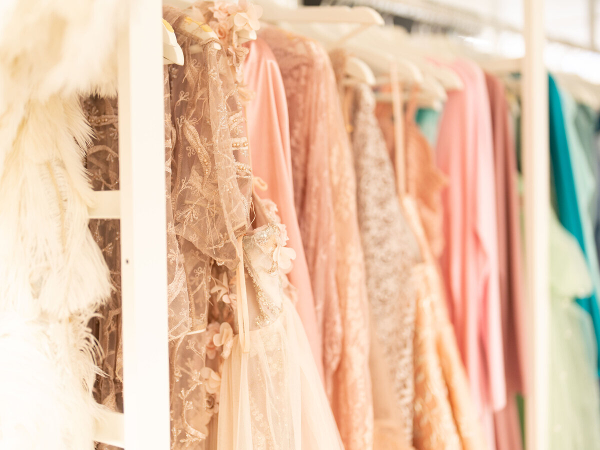 Elegant pastel dresses on hangers in a softly lit wardrobe. Lacy textures and delicate floral accents create a romantic, dreamy atmosphere.