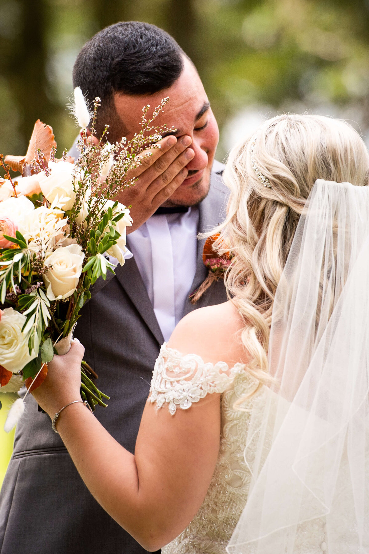 Ottawa wedding photography of a groom in a grey suit wiping a tear away as he sees his bride for the first time