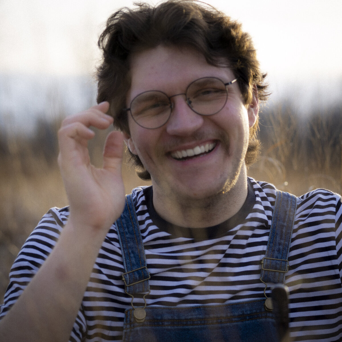 Promotional headshot of a musician in overalls smiling in the grass.