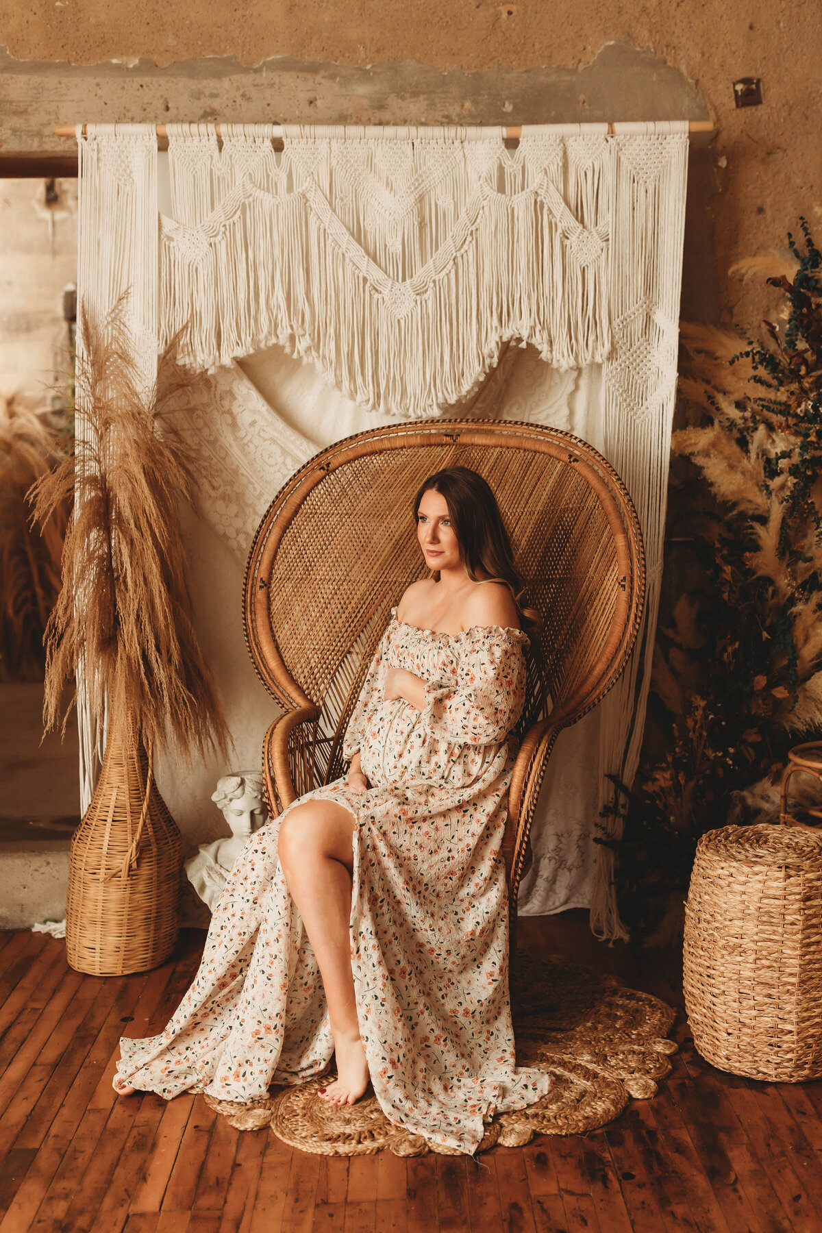 Expecting mother sits in a peacock chair wearing a beautiful floral dress at Dear Meraki Studio Dallas.