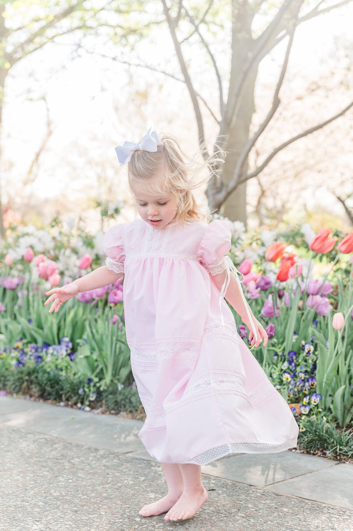 Preschool aged girl dancing in a pink heirloom dress at the Dallas Arboretum in front of tulips.