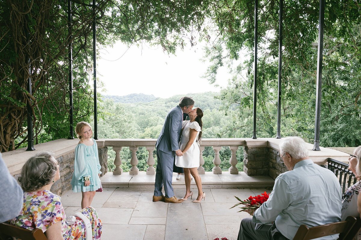 Couple gives kiss at elopement while friends and family look onward with joy.
