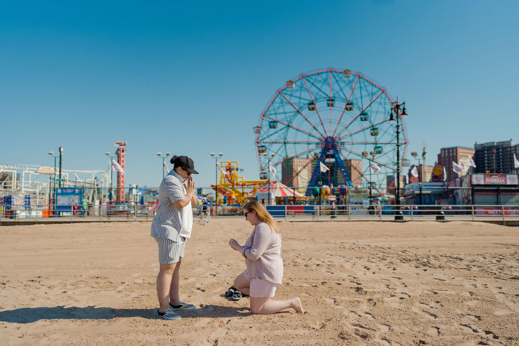 woman kneeling down at the beach proposing to her partner