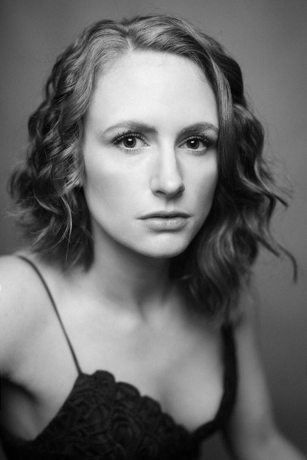 Black and white studio portrait of a woman in an elegant beauty pose, captured in an editorial style.