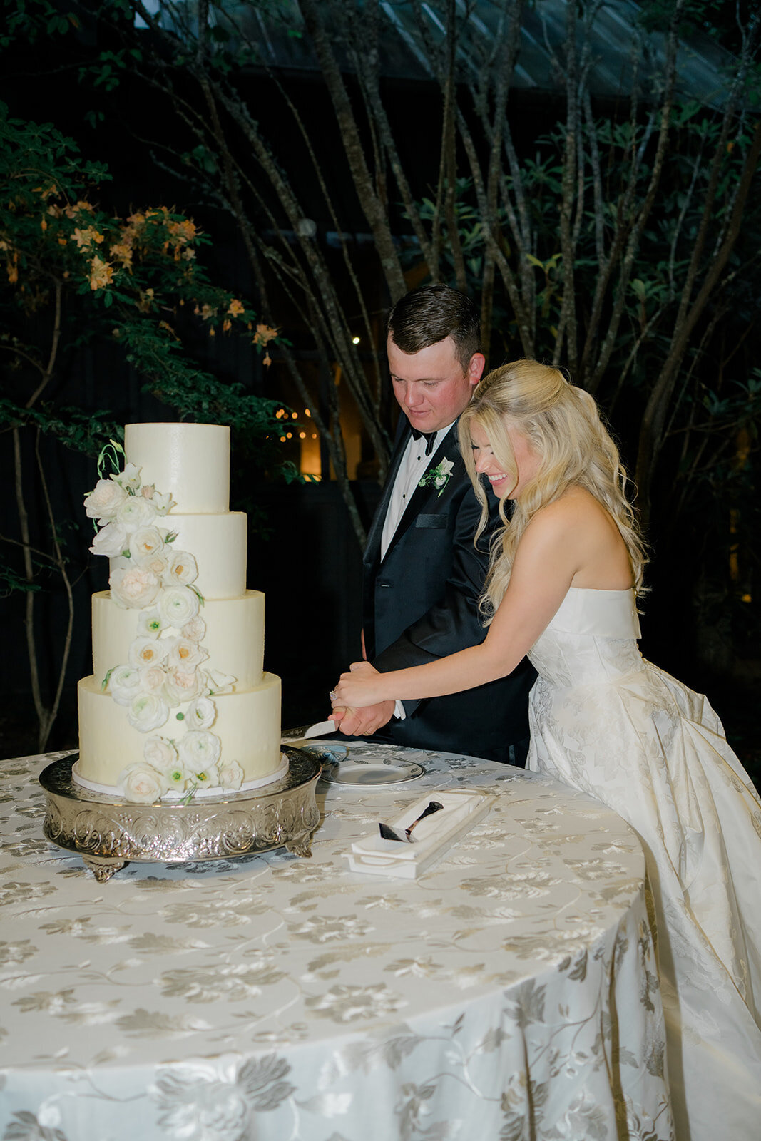 Bride and groom cutting a tall white tiered wedding cake adorned with cascading white flowers at Old Edwards Inn.