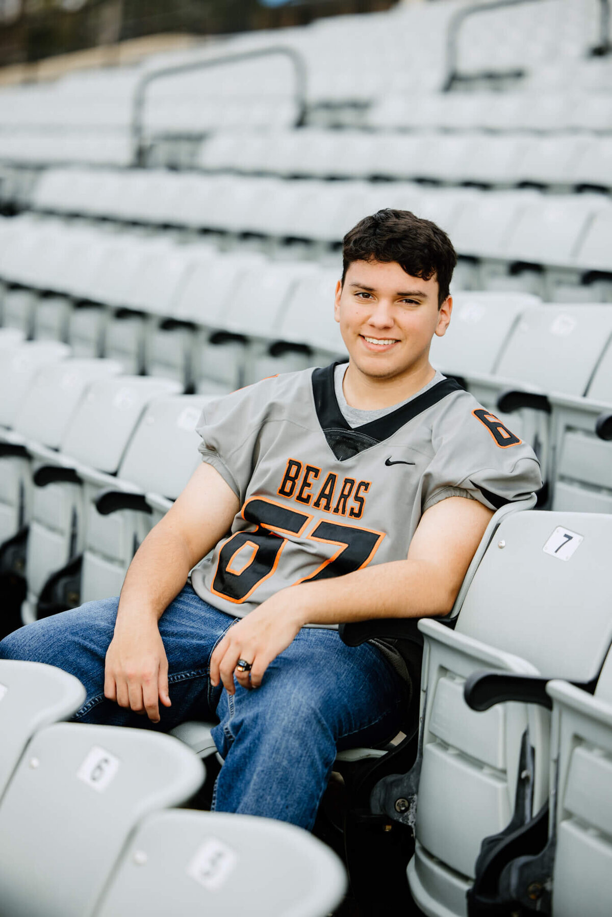 senior boy in football jersey sitting in Gladewater high school football stadium