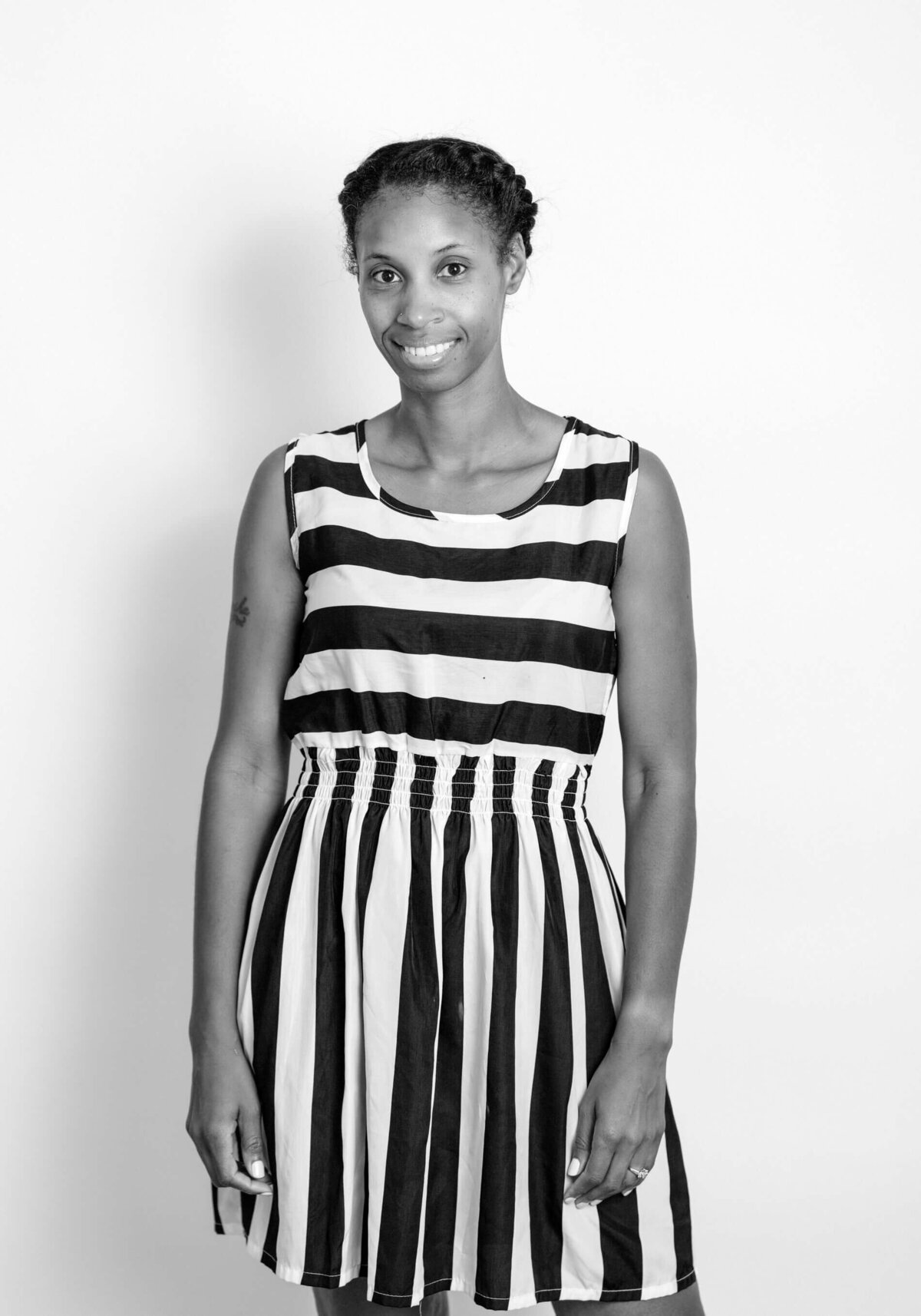 Black and white before shot of a woman in a striped dress, smiling with her hands at her sides.