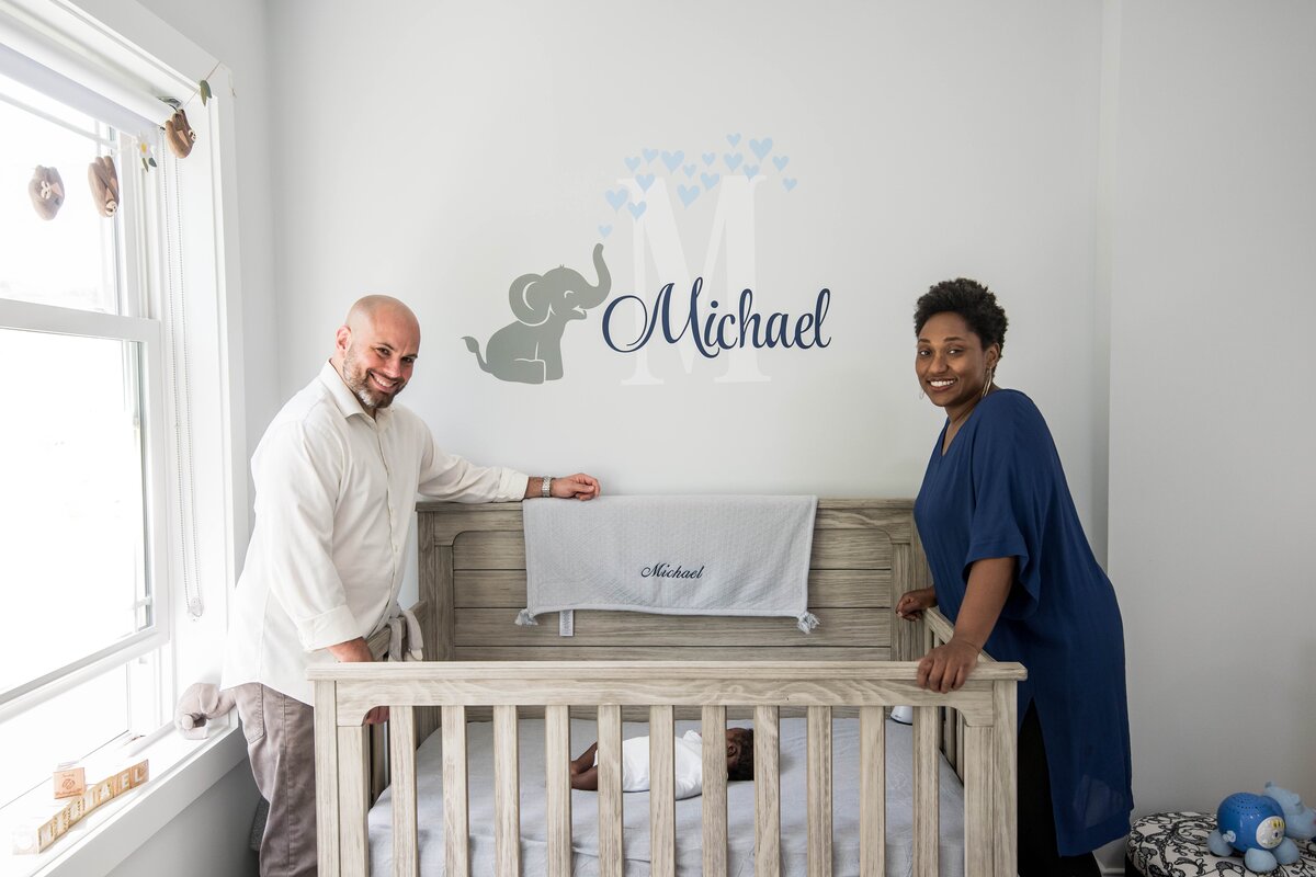 a mother and father lean over the crib of their baby for newborn photography