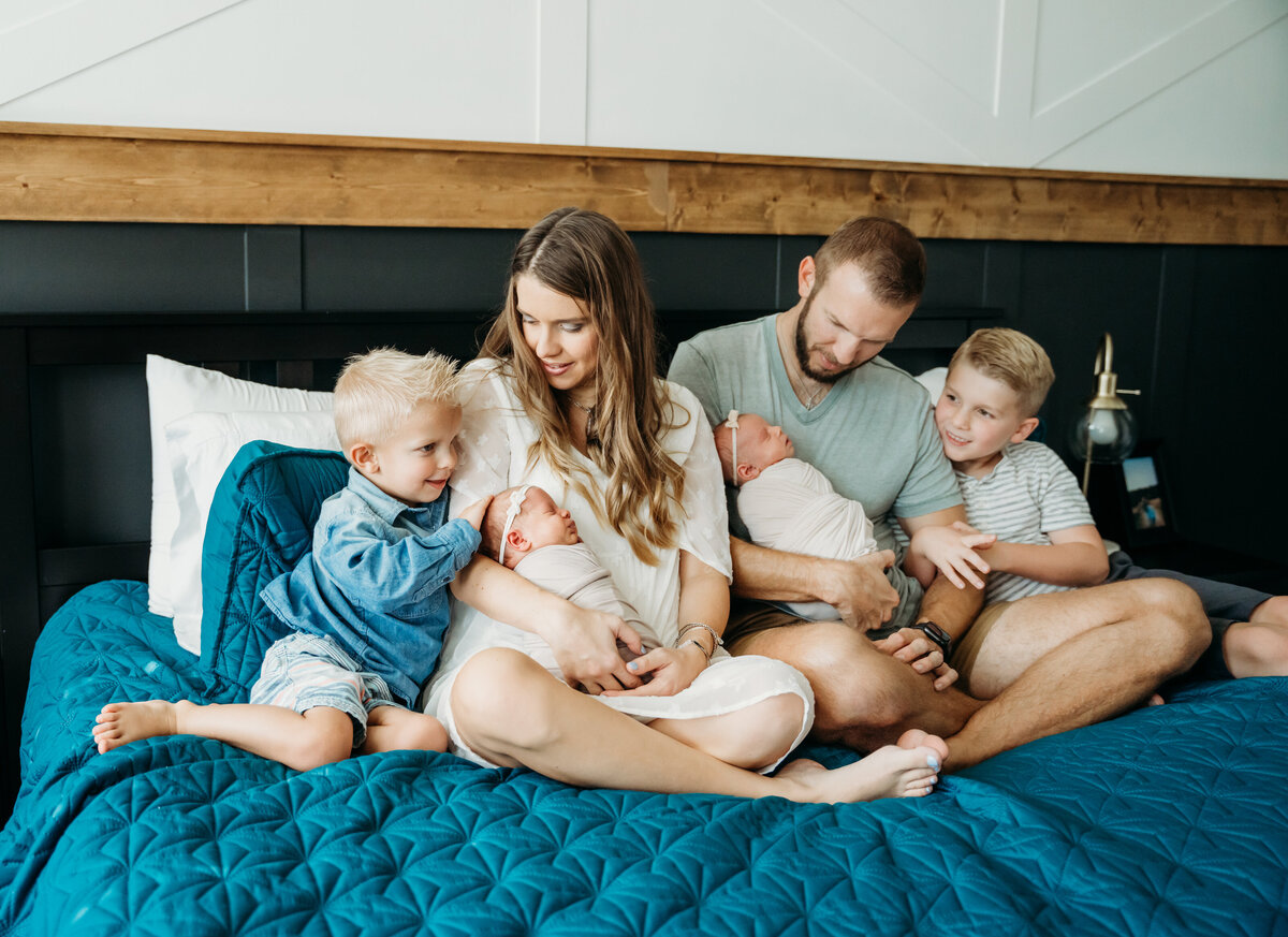 Newborn Photographer, a young mom and dad sit on the bed with their two sons and new twin babies