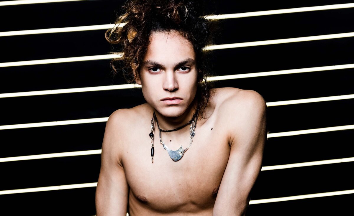 Male musician portrait Tacboy shirtless against black backdrop with white thin light running diagonally across