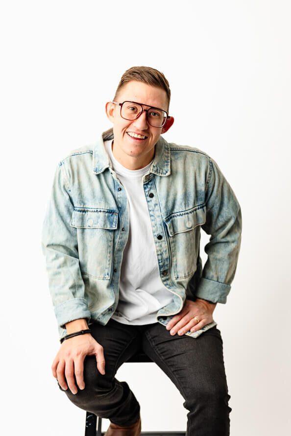 Man in white photo studio puts hands on legs and smiles for camera.