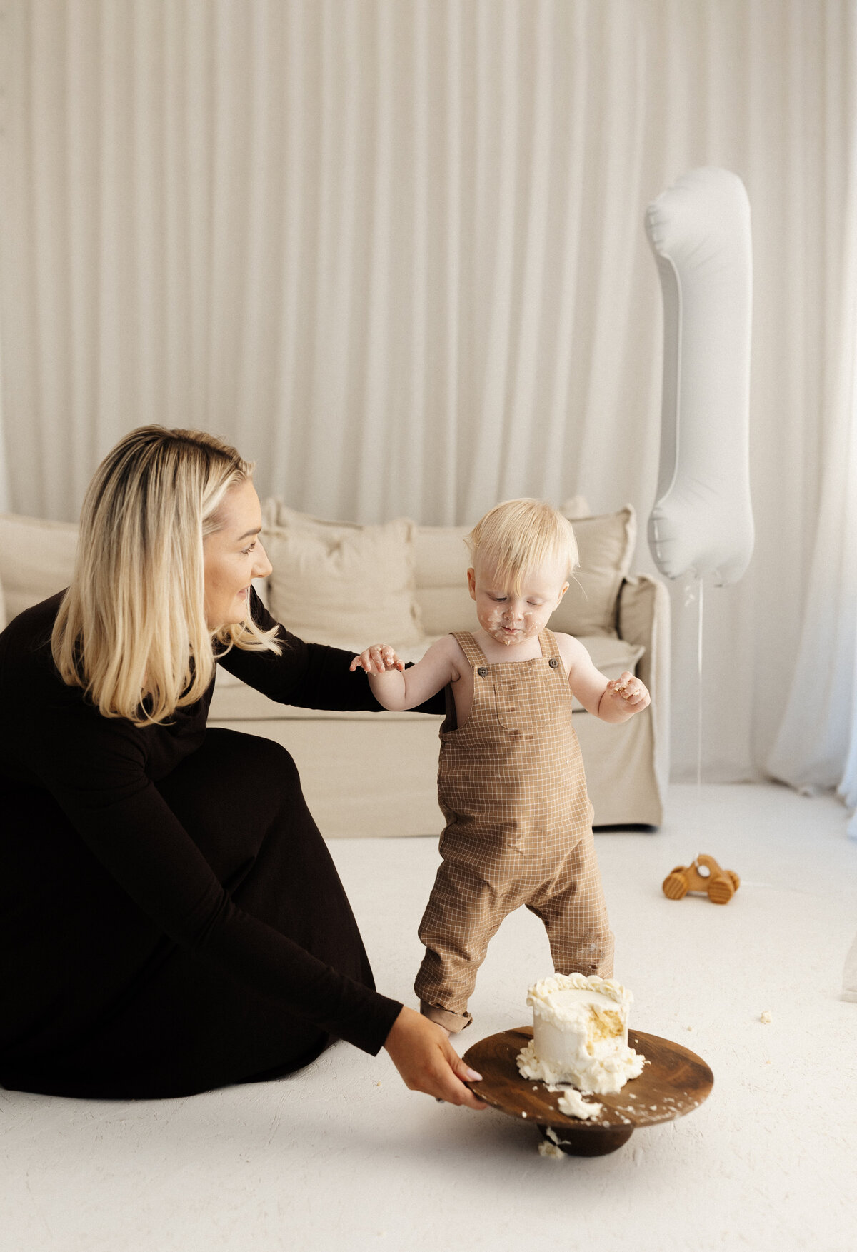 A baby standing up while held by his mother after smashing his first birthday cakesmash