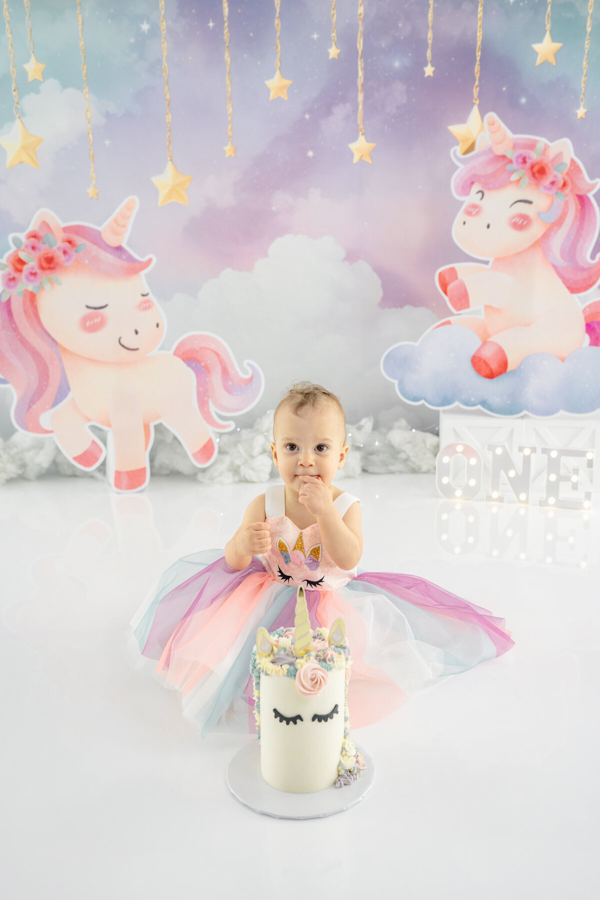 Girl in unicorn dress eating unicorn cake during themed cake smash session— captured by Alliston and Barrie cake smash photographer.
