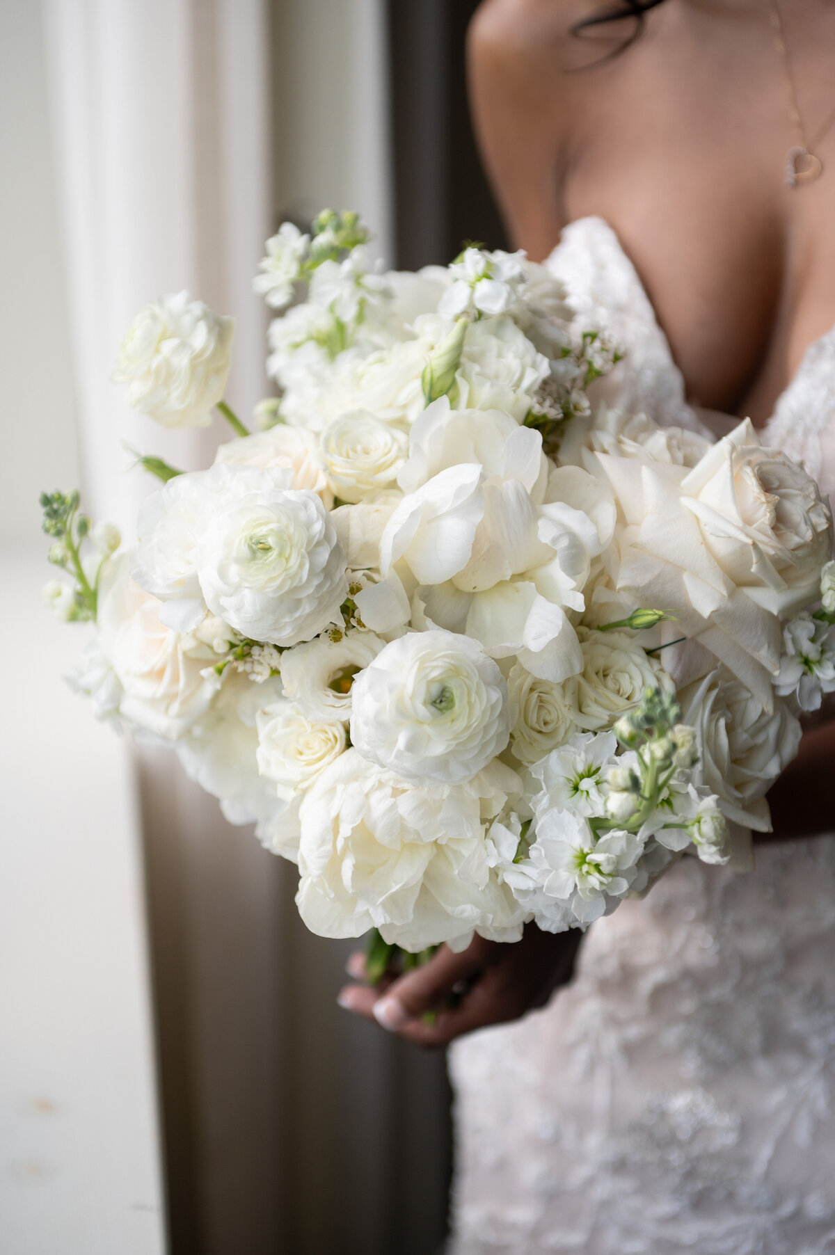 Close-up of an all white bridal bouquet featuring white roses, ranunculus, and greenery, complementing the bride’s elegant lace dress.