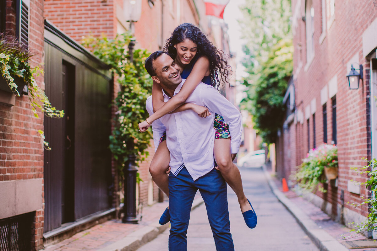 A couple giving a piggyback ride in a narrow street in boston during their engagement session