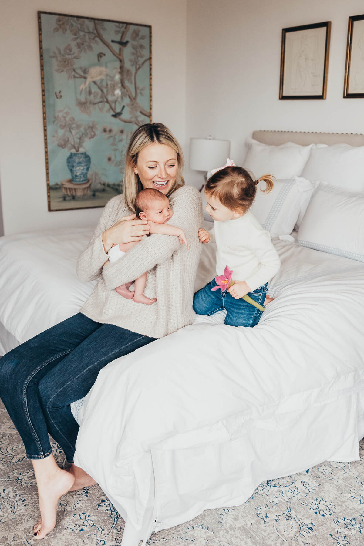 a mother holds her newborn baby while her toddler looks at them both