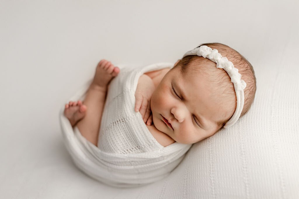 6 day old baby girl posed on a white fabric in denver studio for newborn photos