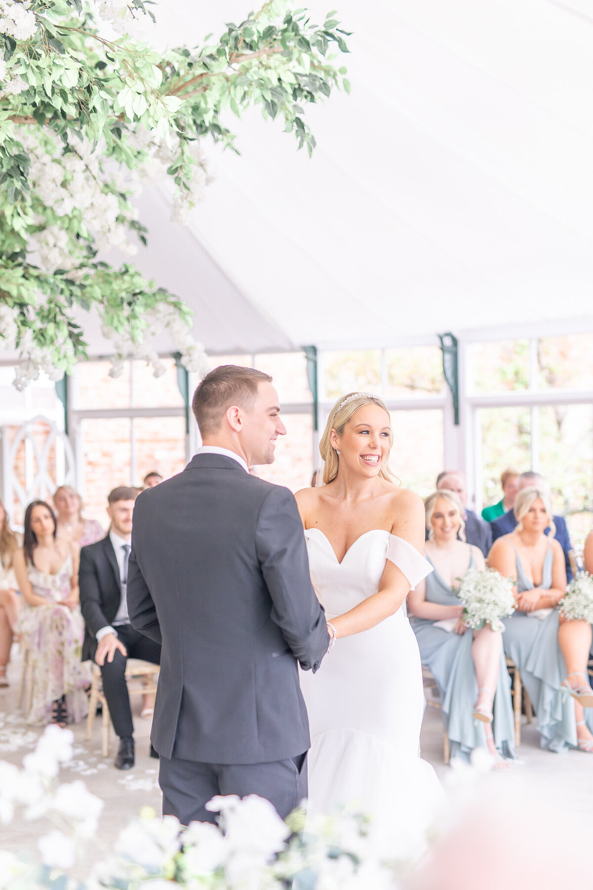 Bride and groom facing eachother holding hands during their ceremony in the glass house