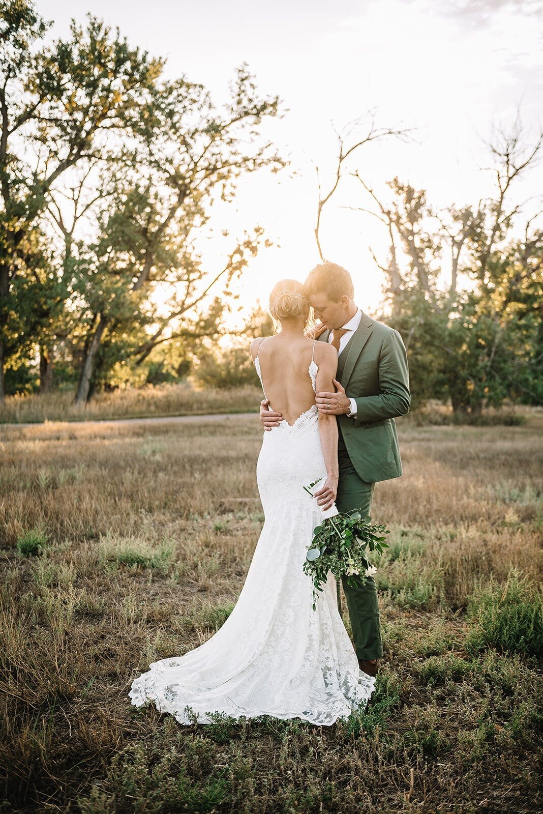 Bride and groom pose on their wedding day during sunset in Colorado with a white and green bouquet.