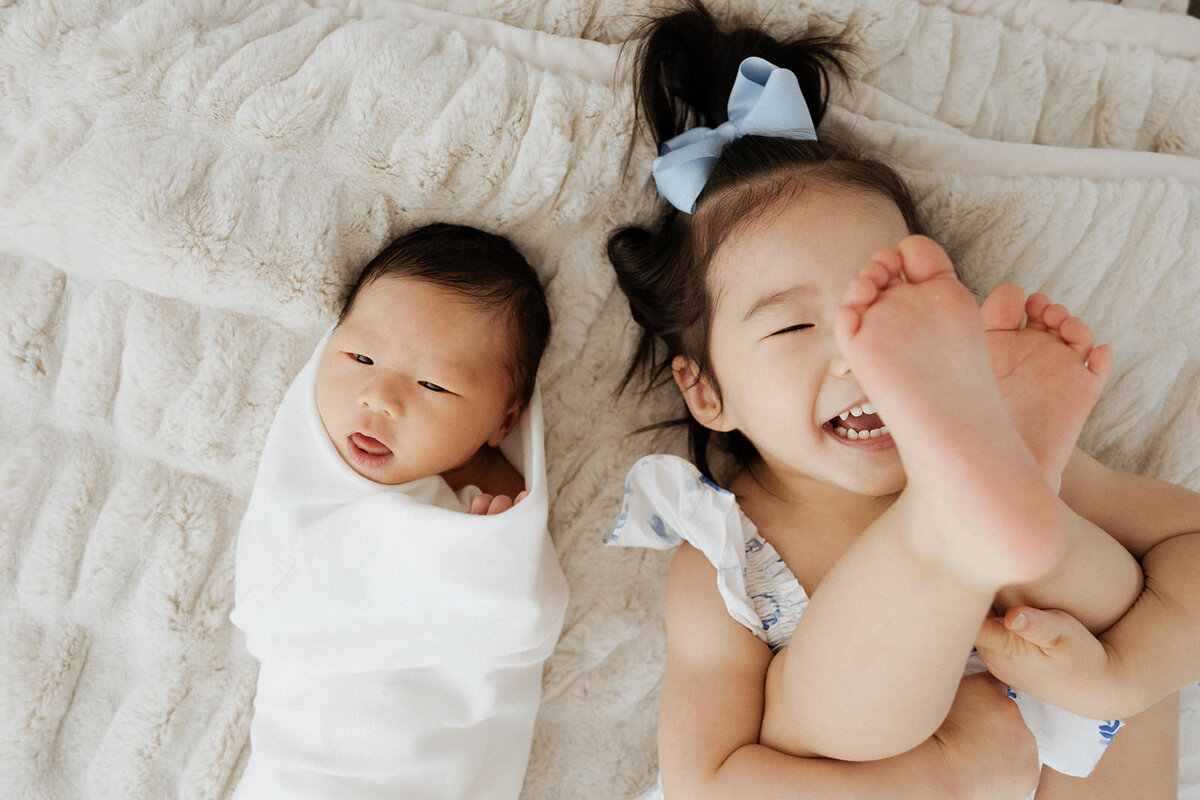 A newborn and a small child laying on a bed next to each other 