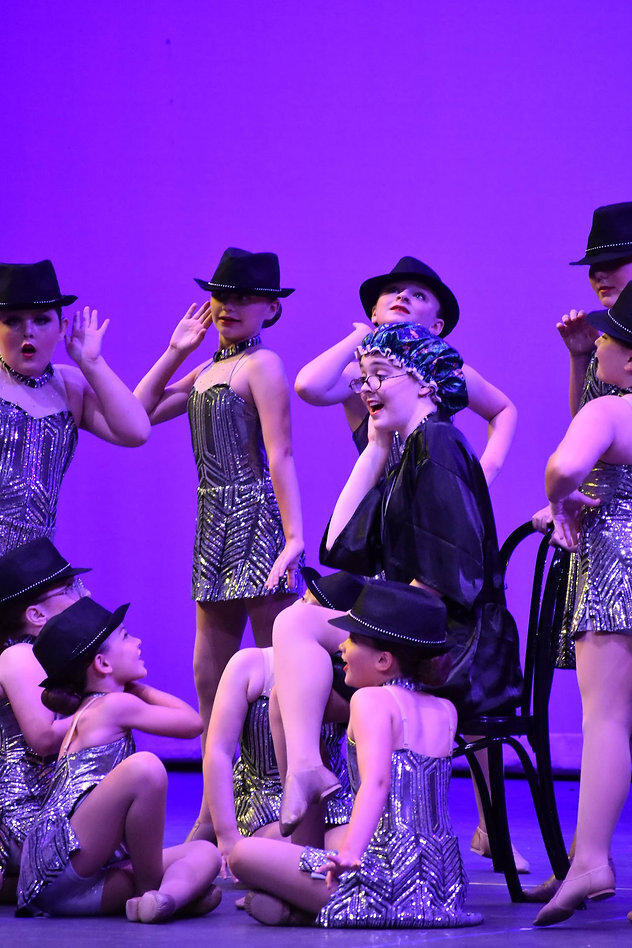 Senior dancer dancing with little girls on stage at recital