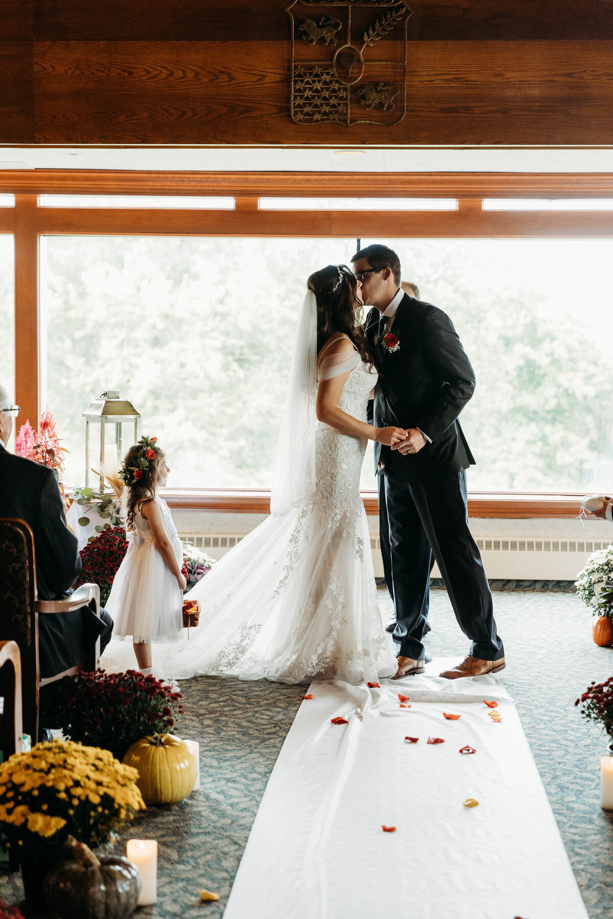Newlyweds kiss to end their ceremony in a large window with flower girl looking on