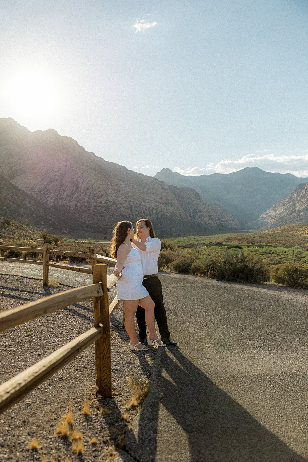 Engaged couple leaning up against fence with Nevada mountains in the back
