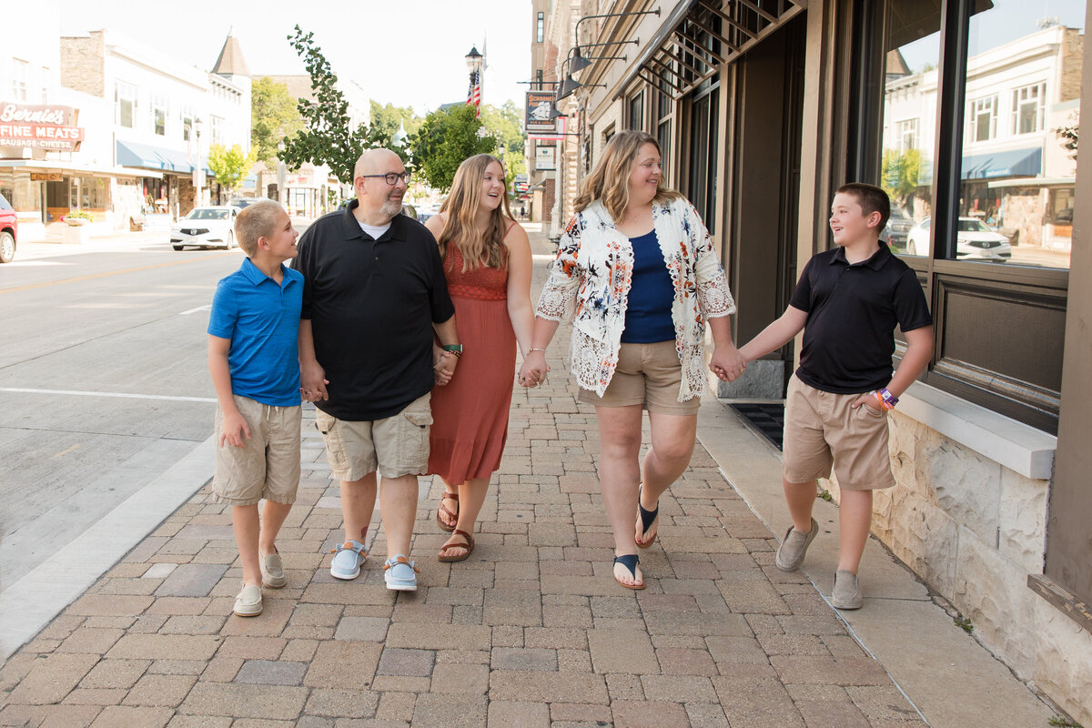 A family is walking along a sidewalk, holding hands and smiling at each other