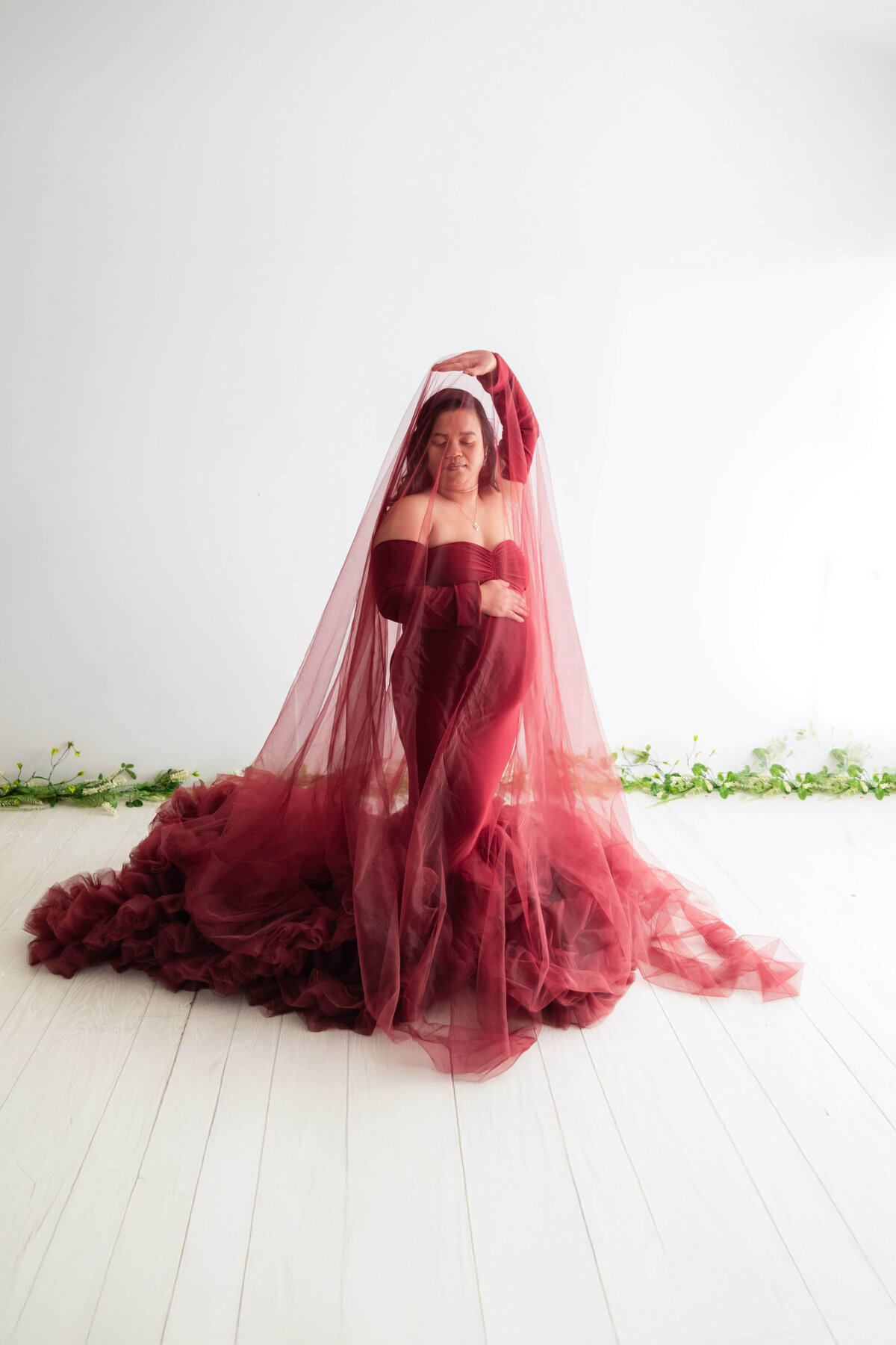 A woman in a red dress and veil sits gracefully on the floor, exuding elegance and poise.