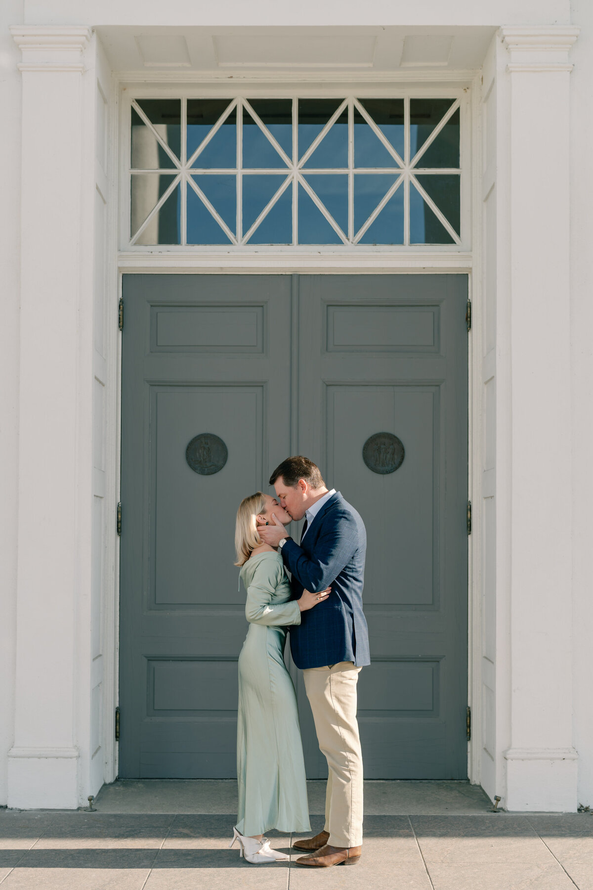 Virginia State Capitol Building Engagement Photos Richmond VA | newly engaged couple in green dress and blue suit share a kiss in front of the door to the Virginia Capitol Building