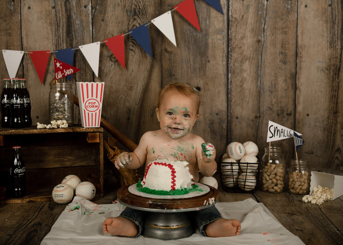 1 year old boy eating his baseball cake. Baseball themed decorations in the background.