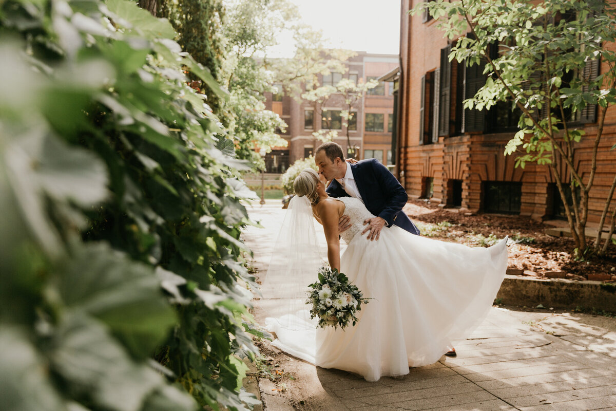 bride and groom kip kiss in the golden light surrounded by greenery in the city
