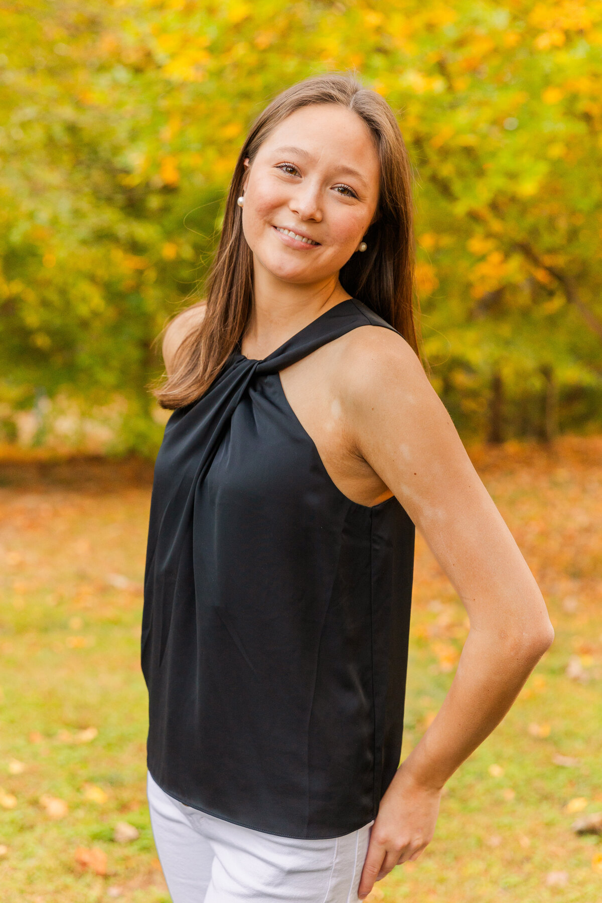 teenager wearing white jeans and a black top smiling at the camera over her shoulder hands in back pockets