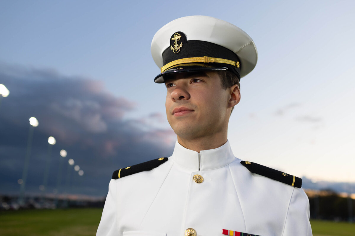 Midshipman on football field at sunset for senior photos at Naval Academy.