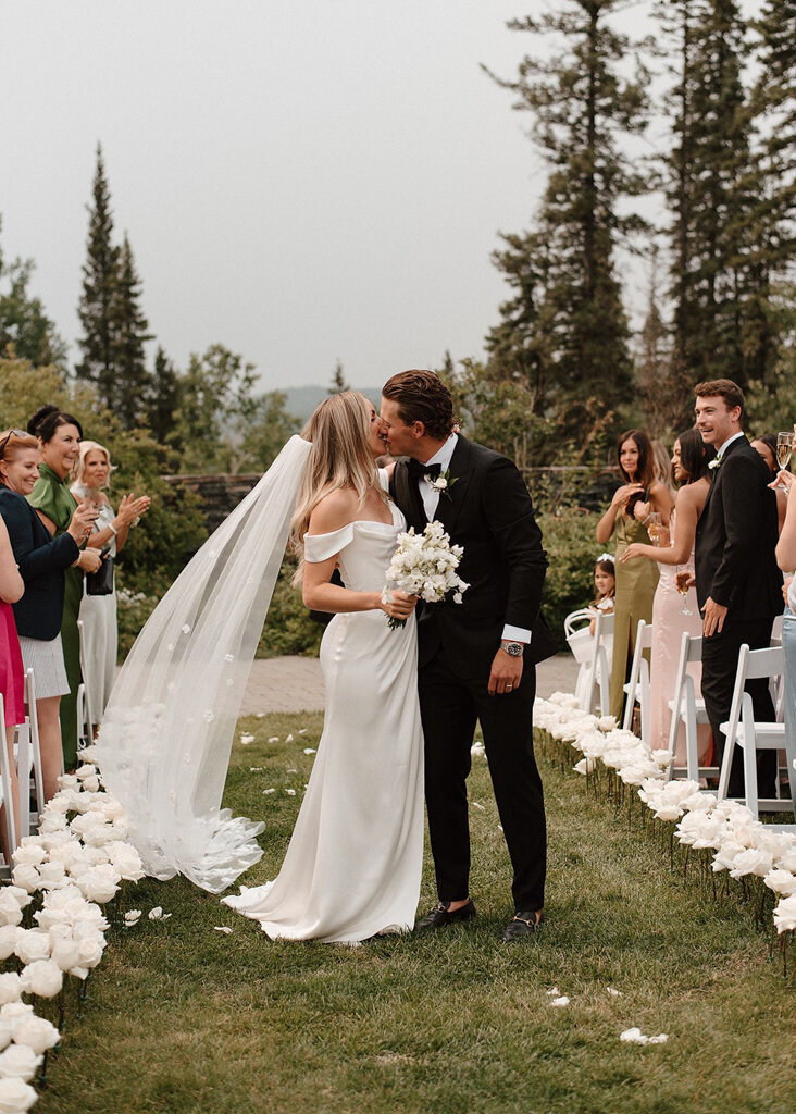 Bride and Groom pause for kiss in the middle of wedding ceremony aisle designed by More Events Co, featured on the Brontë Bride Vendor Guide.